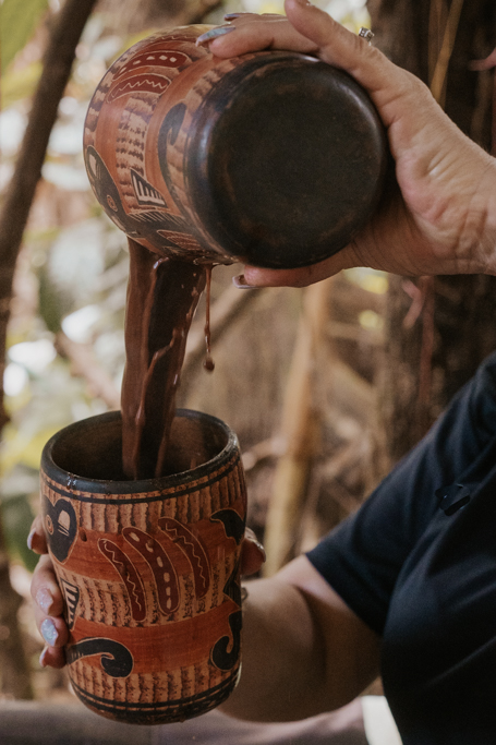 a woman pours hot cacao into a ancient designed cup on a chocolate tour in La Fortuna best things to do