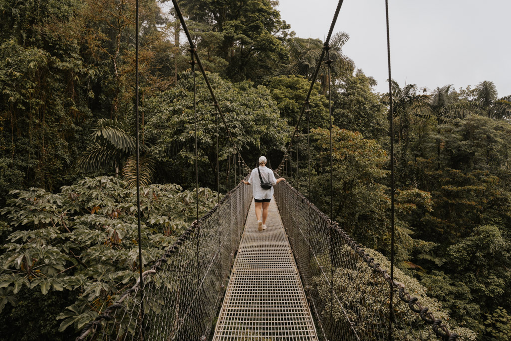 a girl in a white hat and shirt and black shorts walks along a bridge at Mistico Arenal Hanging Bridges in Costa Rica La Fortuna attractions