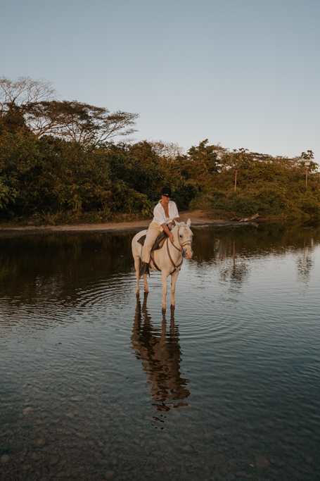 woman on white horse standing in shallow water in Costa Rica