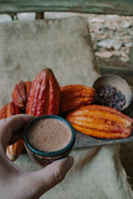 a hand holds a small cup of hot chocolate with orange cacao beans below on one of the best chocolate tour in costa rica La Fortuna