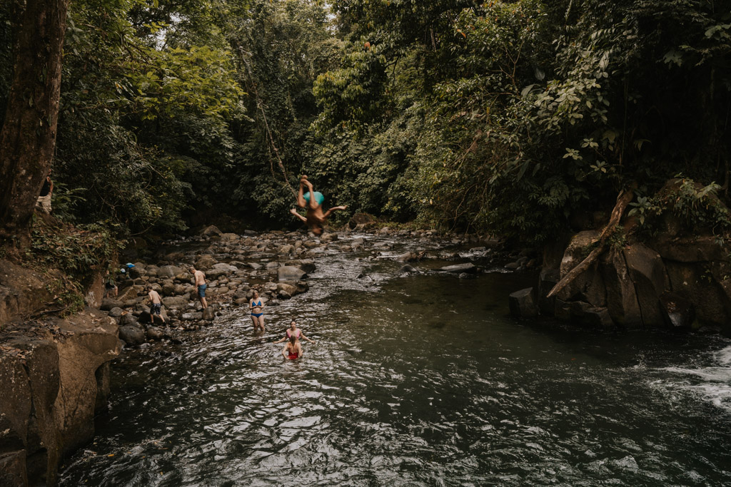 bow in bright blue shorts dives off the El Salto Rope Swing, Costa Rica