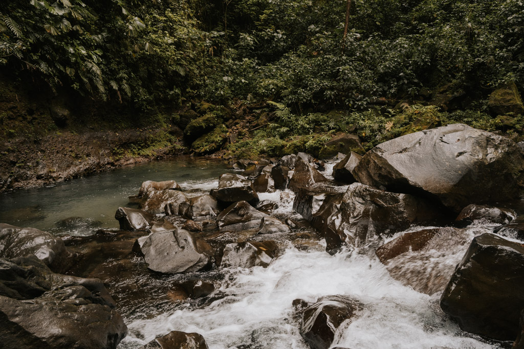 Catarata La Fortuna Costa Rica runs through dark grey rugged rocks to a pool belong with greenery