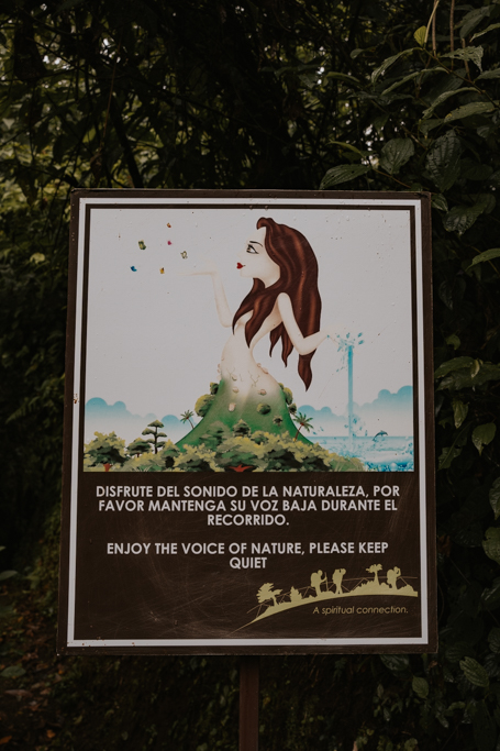 signage with a magical woman and words that say 'enjoy the voice of nature, please keep quiet; in the hanging bridges of arenal attraction