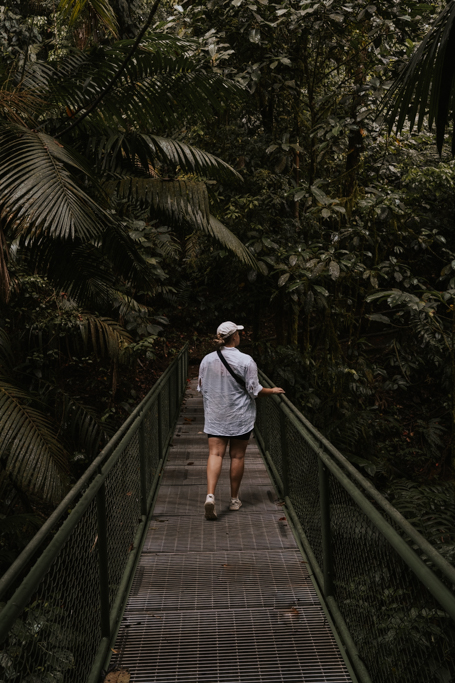 a woman in a white shirt walks along a hanging bridge in Costa Rica amongst rainforest