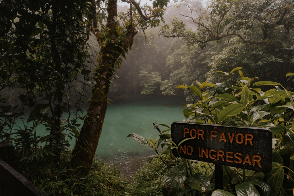 sign that reads 'por favor no ingresar' stands before the blue waters of the river at tenorio costa rica