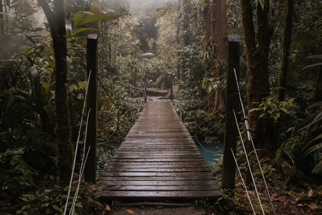a wooden bridge spans over a blue river in tenorio volcano national park