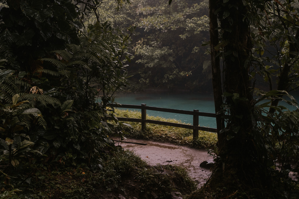 a muddy path in front of a wooden railing and river at tenorio national park costa rica