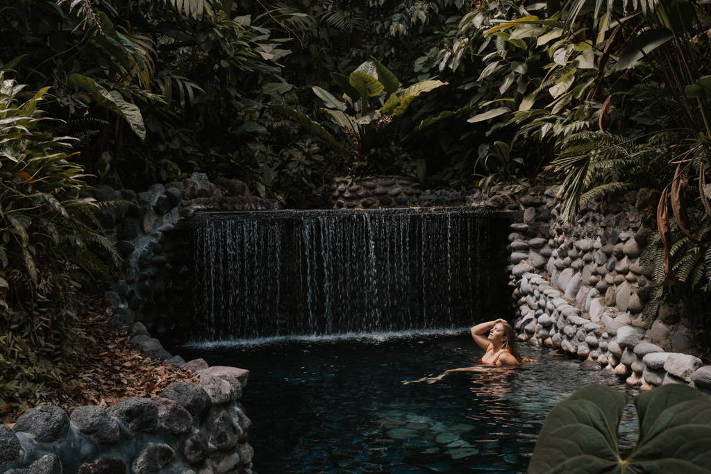 a woman sits in the waterfall at eco termales hot springs Costa Rica