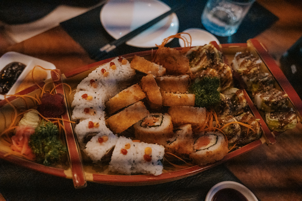 a variety of rolled sushi sit on a red boat dish on a tabletop